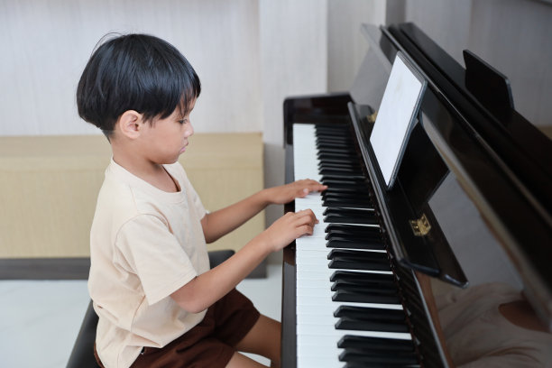 孩子亚洲黑头发男孩坐在和钢琴与平板电脑在客厅的房子室内。音乐和放松使他们快乐。养生生活理念。图片下载