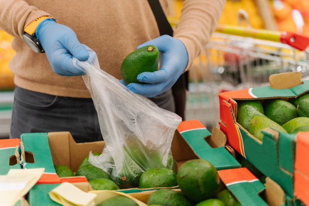 一名男子戴着橡胶防护医用手套，在超市买牛油果，在杂货店选择健康水果，保护自己免受冠状病毒的侵害。检疫、购物图片下载