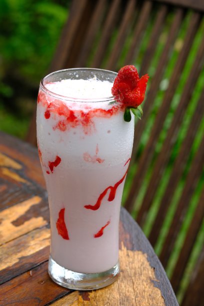 香草奶昔和融化的草莓果酱在一个透明的杯子里，放在木桌上。图片下载