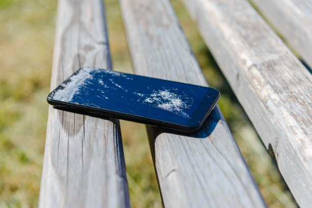 在公园的木凳上摔坏了手机。屏幕破碎的智能手机。夏日公园，特写。图片下载