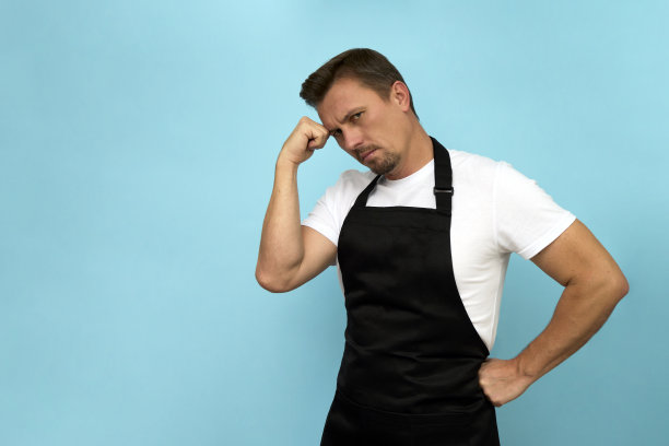 年轻的咖啡师穿着黑色围裙和蓝色背景的白色t恤图片下载