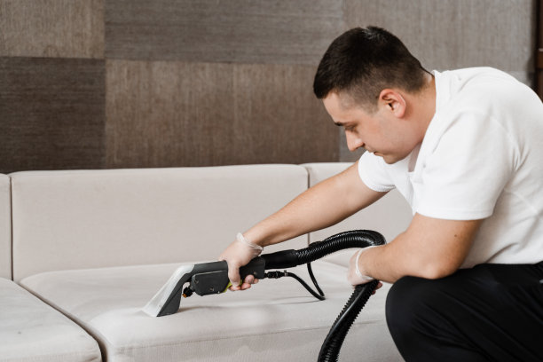 管家正在用干洗机提取软垫沙发上的污垢。吸尘器是清洁沙发与洗涤真空吸尘器抽干机干洗软垫家具。图片下载