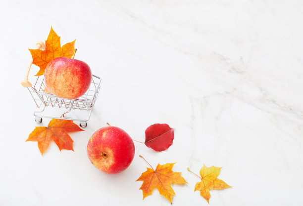 小推车里的红苹果和白色大理石背景上的枫叶图片下载