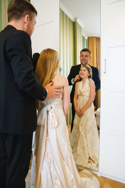 爸爸和穿着妈妈婚纱的金发小女孩站在镜子前。图片下载