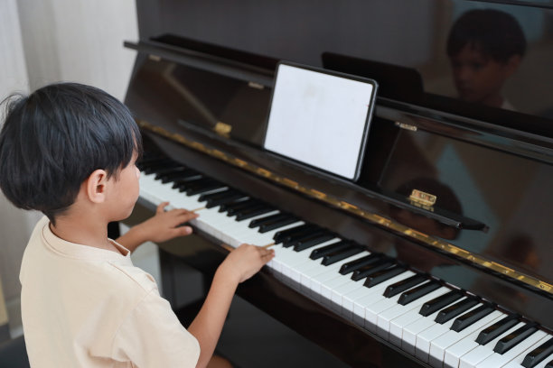 孩子亚洲黑头发男孩坐在和钢琴与平板电脑在客厅的房子室内。音乐和放松使他们快乐。养生生活理念。图片下载