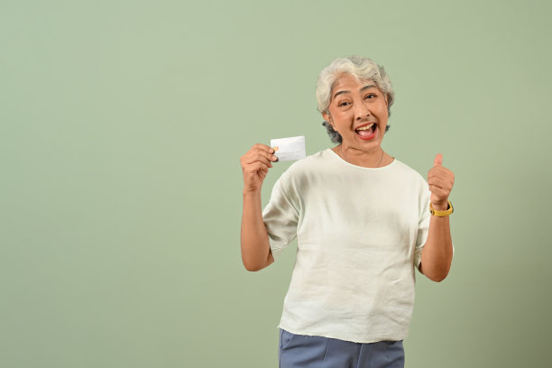 兴奋的白发老妇人拿着信用卡，孤立在柔和的绿色背景上。图片下载