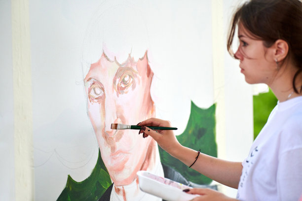 在艺术绘画节上，年轻的女孩艺术家在白色画布上用画笔画出男人的肖像图片下载