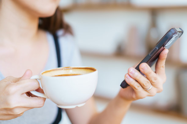 在咖啡店里一边喝咖啡一边用智能手机的女人。图片下载