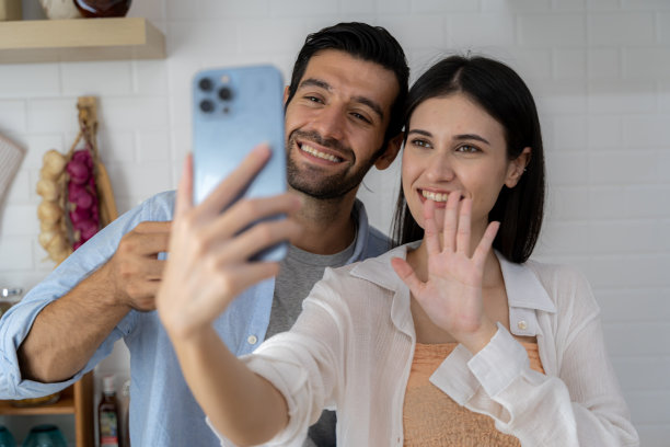 管家在休息时自拍，用手机，年轻夫妇对着相机拥抱微笑，站在清洁工具和用品的地板上，厨房内部。图片下载