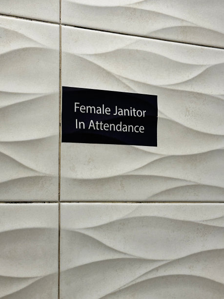 黑色矩形标志的特写图像，上面写着白色的“女看门人值班”，贴在公共厕所的瓷砖墙上，白色的瓷砖有纹理的波浪图案图片下载