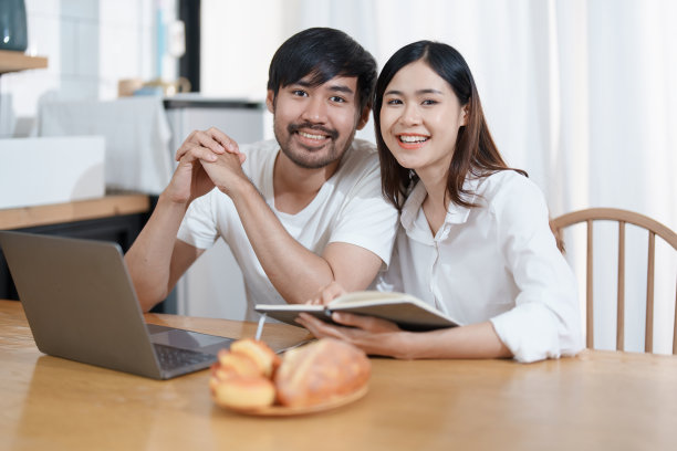 年轻的夫妇露出幸福的笑容，在家里放松，用电脑和笔记本计算家庭的收入和支出。图片下载