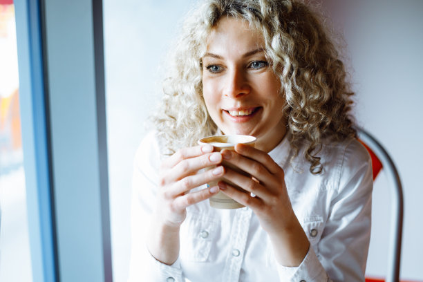 迷人的年轻卷发女商人在工作休息时享用咖啡的肖像。咖啡休息。休息和快乐。积极的情感。一个好心情。快乐的人。图片下载