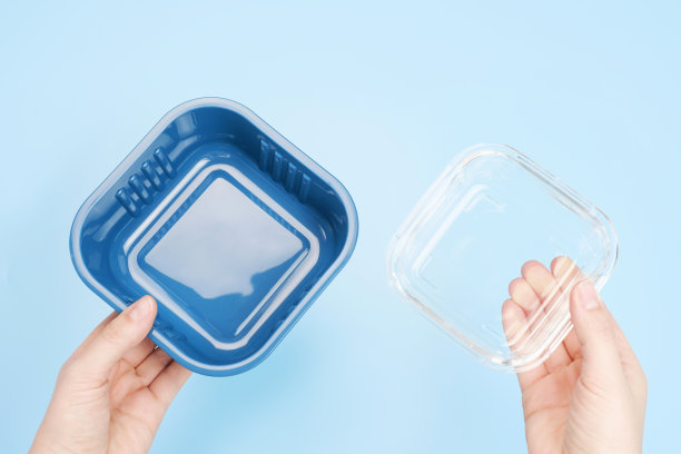 一只女性的手从上方拿着一个蓝色背景的玻璃和塑料盒子。图片下载