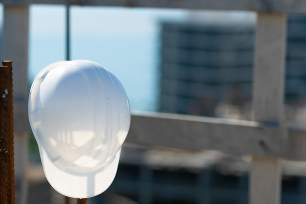 一个阳光明媚的日子里，建筑工地的钢筋上挂着一个白色头盔的特写。施工理念，安全技术图片下载