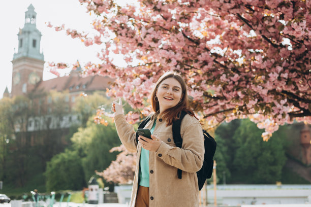 美丽时尚的女人走在春天的一天，拿着手机在街道背景。红发女孩指指点点。电话沟通。城市生活方式概念。查看社交网络图片下载