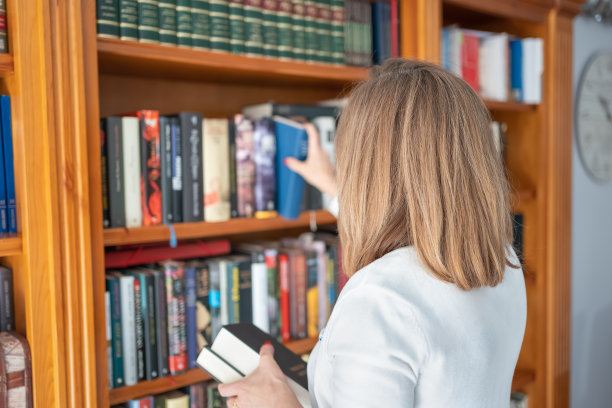 一个背朝前的金发女人从书店里挑了一本书。图片下载