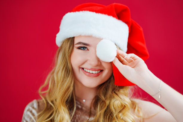 一个身材苗条的美女，头戴圣诞老人帽，背景是红色的。图片下载