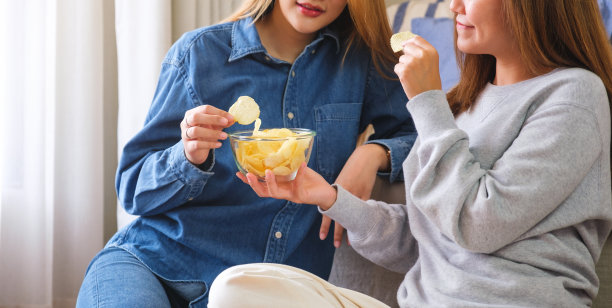 一对妇女一起分享和吃薯片的特写照片图片下载