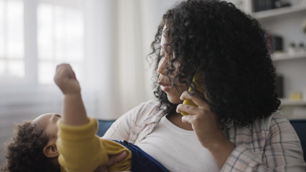 当妈妈打电话的时候，小男孩在妈妈的手里哭泣，产假，育儿图片下载