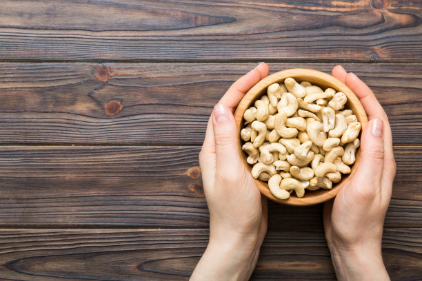 女人的手拿着一个装有腰果的木碗。健康食品和零食。各种坚果的素食小吃图片下载