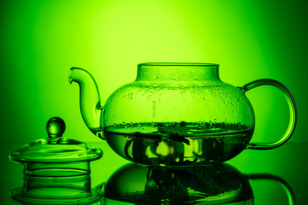 玻璃透明茶壶与草药茶和绿色梯度背景上的一个开放的盖子。健康食物概念图片下载