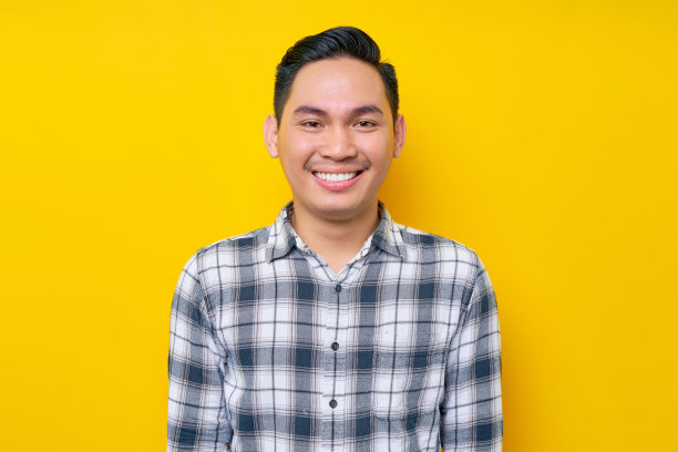 近距离镜头:一个穿着格子衬衫微笑着的年轻亚洲人，在黄色的背景中带着自信的表情看着镜头。人们的生活方式理念图片下载