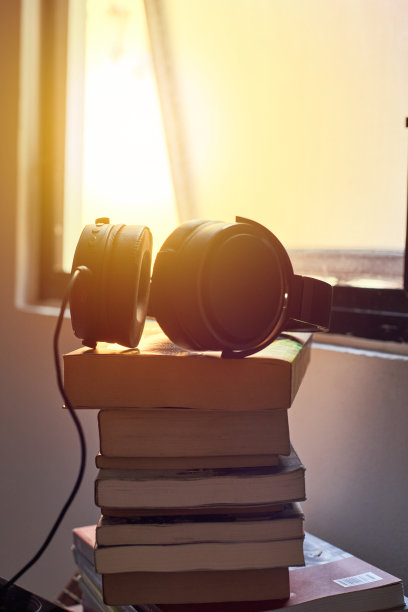 把耳机放在桌上的书上，背景是阳光。概念有声读物、电子学习、教育、文学。图片下载