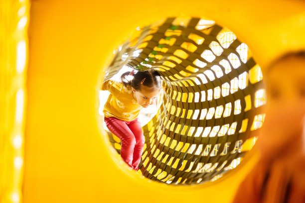 小女孩在黄色操场公园的活跃娱乐活动中移动管道。图片下载