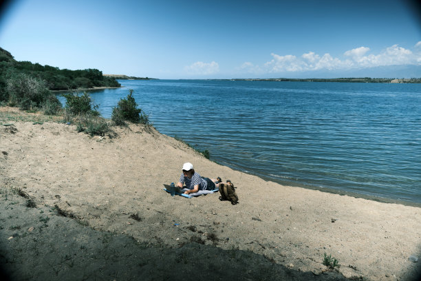 女游客躺在湖滩上，用笔记本电脑交流图片下载