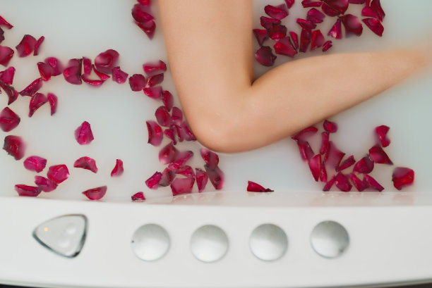 女人躺在有牛奶和玫瑰花瓣的浴缸里。图片下载