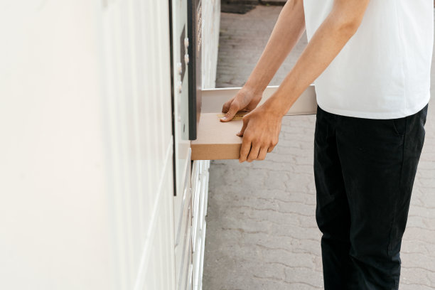 在自助邮件终端机附近，一名男子手里拿着一个盒子。包裹投递机。拿着纸板箱的人。邮件投递和邮政服务，网上购物，电子商务的概念图片下载