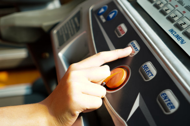 图片显示一只手按下跑步机控制面板上的启停开关按钮。图片下载