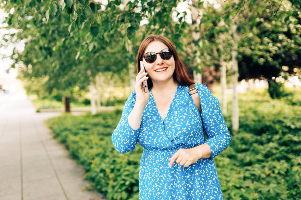 美丽的微笑女性讲电话，站在外面。电话沟通。走在城市街道上的快乐开朗的年轻女子，都市生活方式的概念。旅行者图片下载