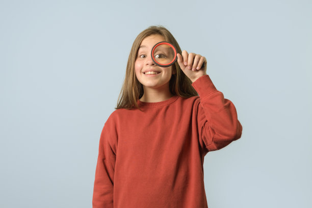 年轻的研究员。一个好奇的女孩拿着放大镜的肖像。红毛衣，浅蓝色背景图片下载