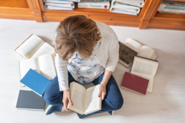 一个白人妇女坐在地板上，头顶上有一张照片，上面有很多书图片下载