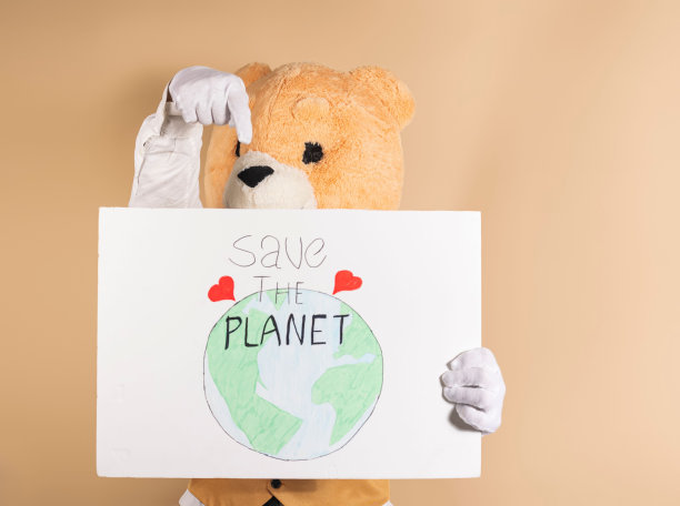 一名男子戴着黄色背景的泰迪熊面具，手持写着“拯救地球”的纸板图片下载