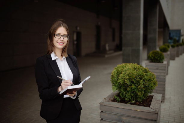 一位身穿职业装、戴眼镜的女士在笔记本上做笔记。图片下载