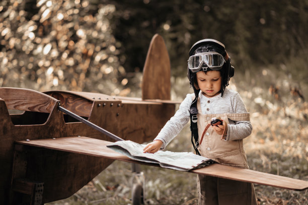 一个年轻的飞行员男孩带着指南针和地理地图在自然景观中靠近一架自制飞机。画面的真实情绪。制图。古董。图片下载