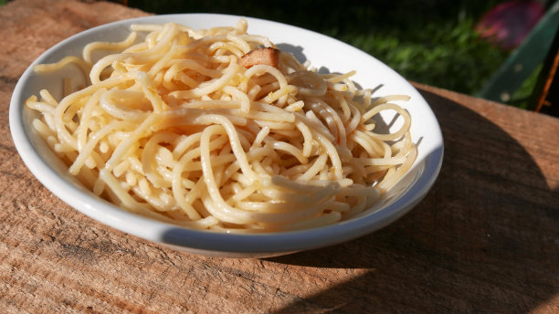 面。在后院的午餐桌上，在阳光下。午餐盘，侧视图，特写:桌上的培根意大利面。培根意大利面。橄榄油意大利面。吃面条。吃意大利面条。表侧视图。阳光下的午餐图片下载