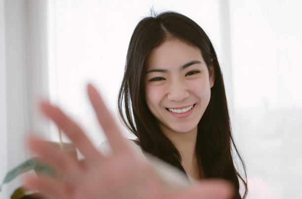 漂亮的年轻亚洲女人穿着白色t恤，友好地微笑着站在卧室。韩国女孩在模糊的背景下愉快地自拍。度假活动和生活方式概念。图片下载