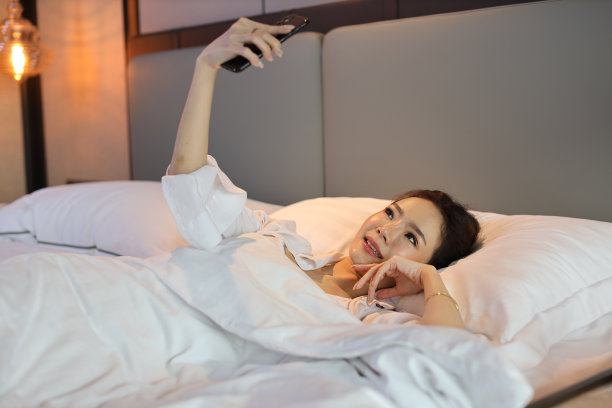 俯视图年轻美丽的亚洲女人穿着白色睡衣躺在床上自拍，在做好梦之前用手机打招呼。生活方式的概念图片下载
