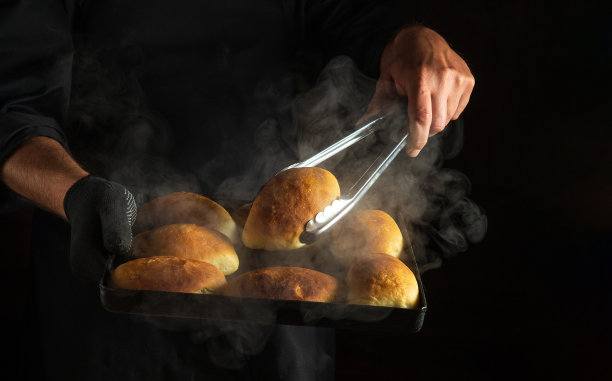 面包师在从烤箱中取出的热烤盘上烤馅饼或面包。菜单或食谱的黑色空间。图片下载