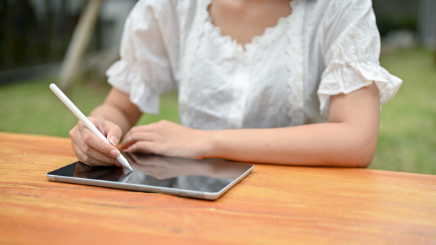 一位女性在户外的桌子上使用她的电子平板电脑的特写照片。图片下载