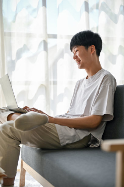 从侧面看，一位快乐的亚洲年轻人正在用笔记本电脑观看社交媒体上的视频图片下载