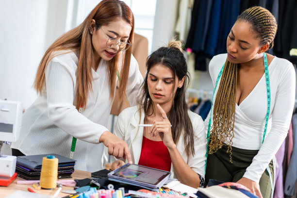 不同的女性时装设计师在裁缝工作室设计服装。迷人的年轻女裁缝师团队感到快乐，享受在车间商店设计新款式的衣服。图片下载