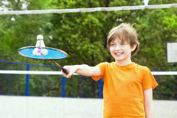 微笑的小运动员打羽毛球。快乐的孩子手里拿着羽毛球拍图片下载