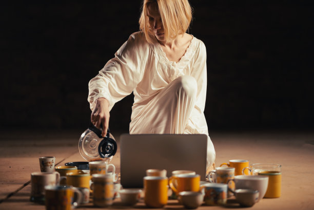 截止日期，回收概念。女人和许多咖啡杯坐在笔记本电脑前。一个黑暗的房间。图片下载