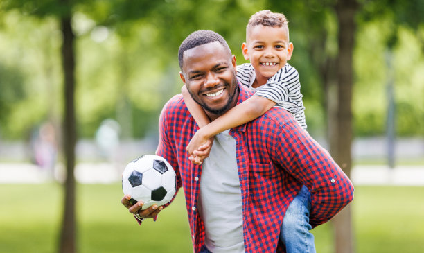 快乐的父亲和儿子在公园的绿草地上踢足球的照片图片下载