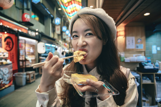 在京都的西木市场，一名亚洲女子正沉浸在日本的美食中，品尝着当地的美食。她沉迷于街头小吃，体验着该地区丰富的风味和文化底蕴。图片下载