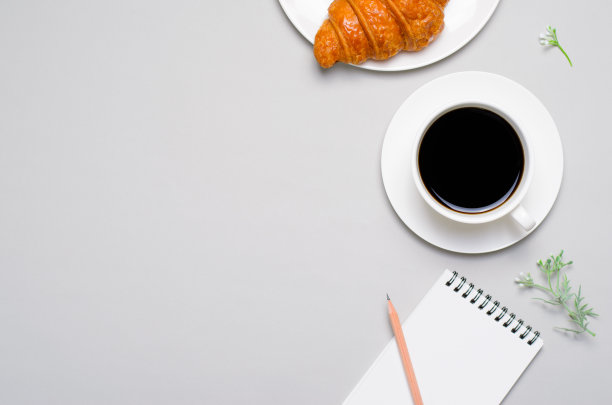 新鲜出炉的羊角面包，一杯咖啡和记事本在灰色背景图片下载